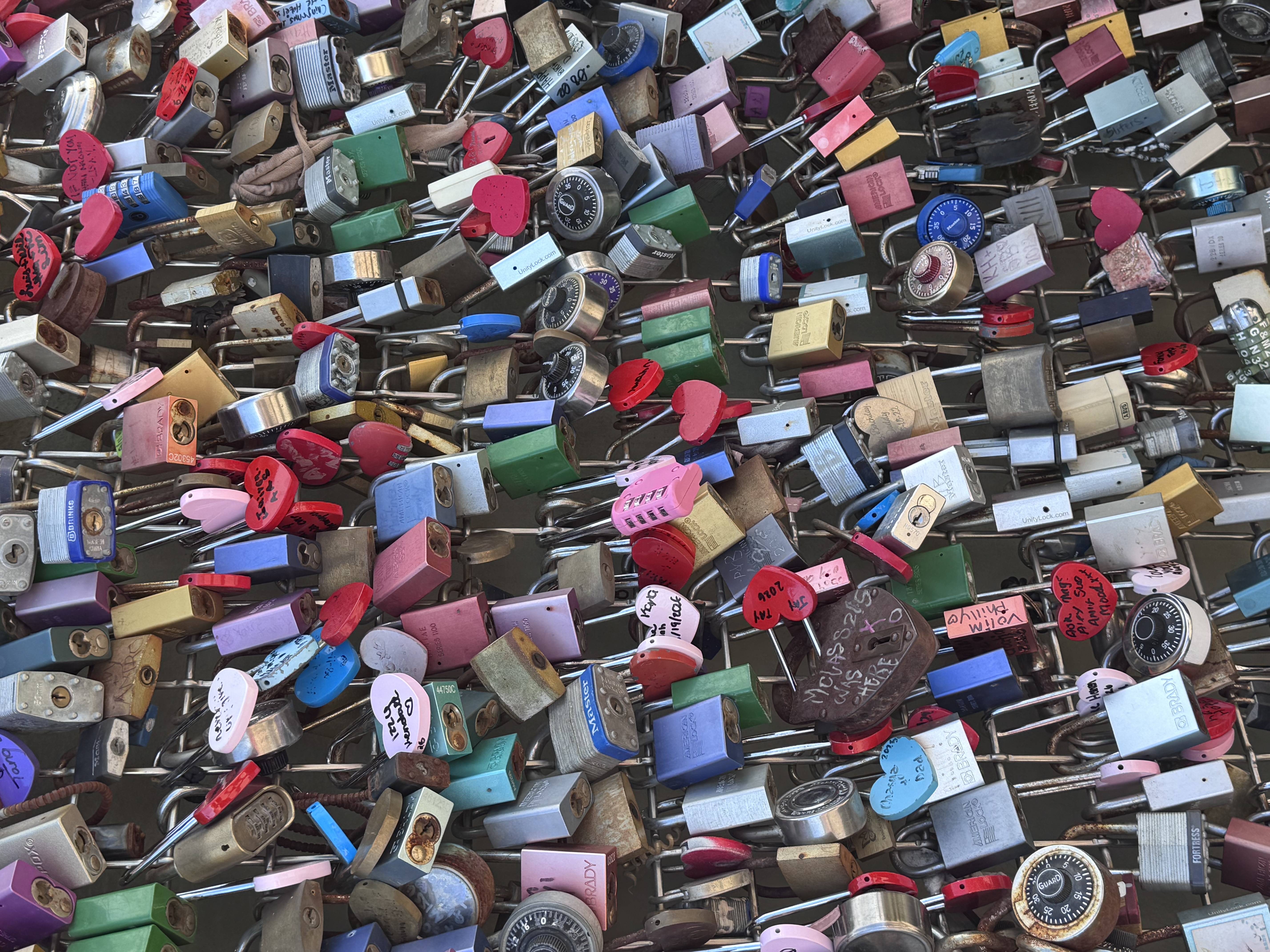 A fence covered in colorful padlocks and painted hearts